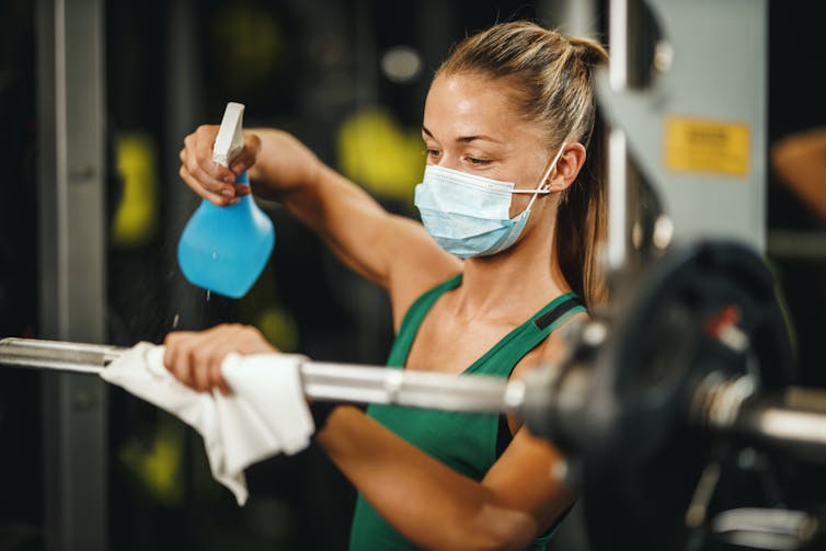 Une sportive, masquée, nettoie les barres qu’elle vient d’utiliser